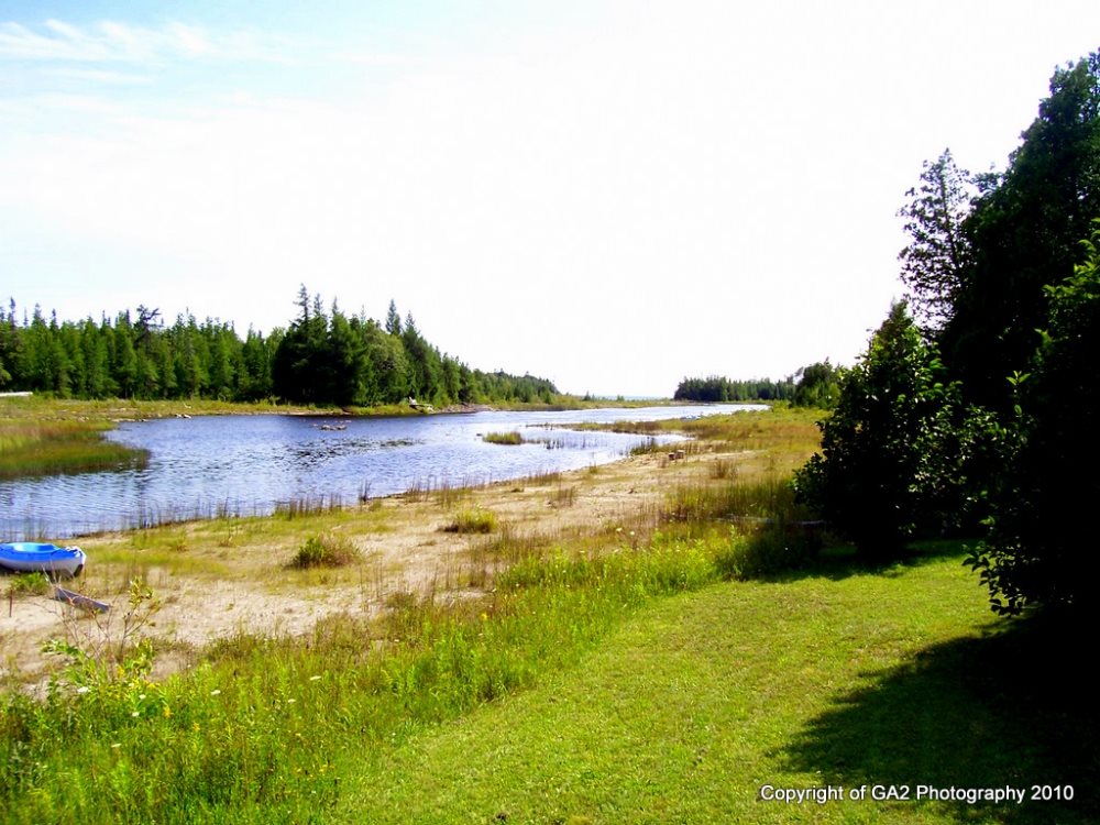 Large front lawn leads to sandy apron that edges the lake water in front of the cottage.