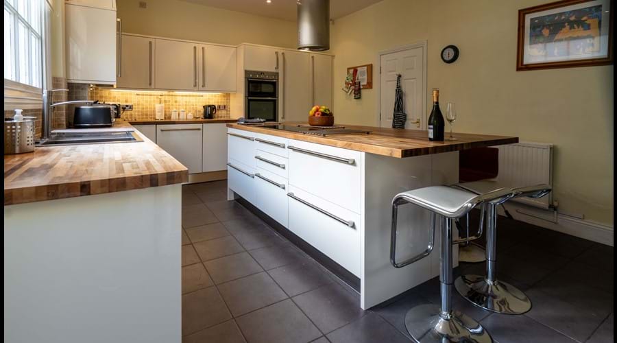 Modern kitchen with large island, barstools, electric hob, double oven, dishwasher, microwave, washer & dryer.
