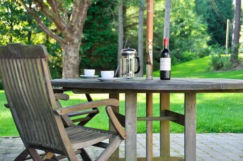 Bottle of red wine and cafettiere of coffee on an outside table in mature gardens