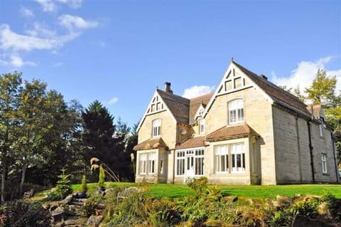 Rothley Lodge, looking up the mature garden towards the imposing stone double fronted house.