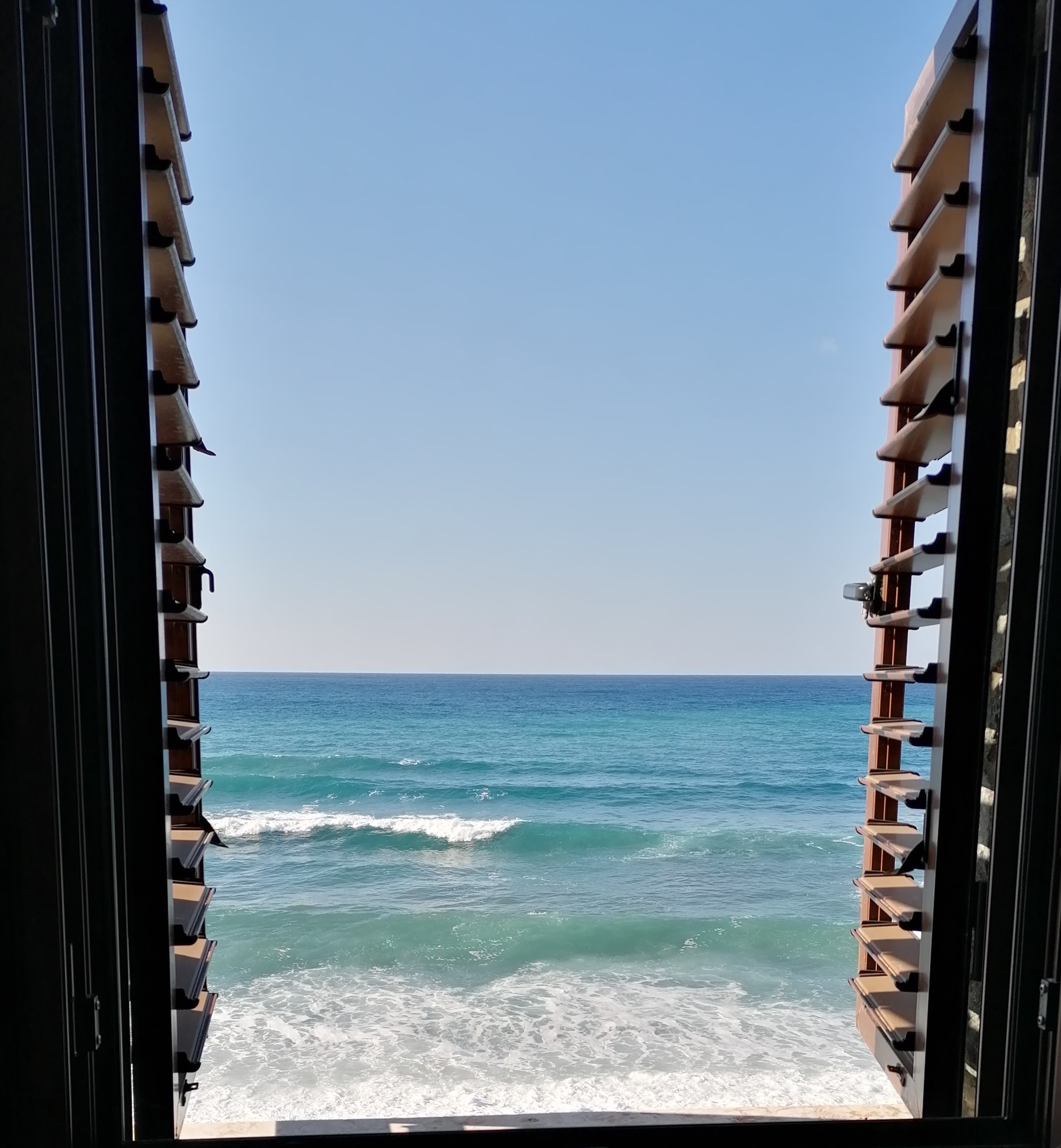 Blue sea and white waves through wooden shutters