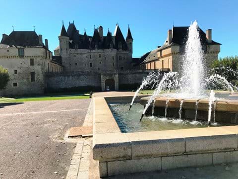 Turreted chateau Jumilhac in the background with a working fountain in the foreground