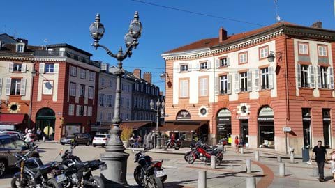 Large square with traffic and surrounded by red bricked buildings and 3 bulb lamp posts in central Limoges 