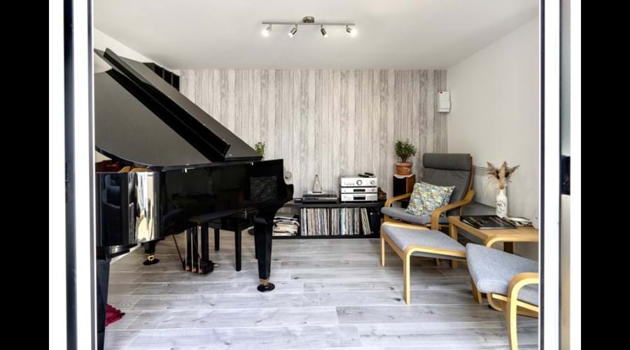 Patio doors to the music room open showing easy chairs, hi-fi and baby grand piano