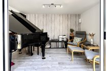 Patio doors to the music room open showing easy chairs, hi-fi and baby grand piano