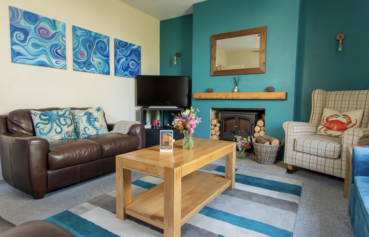 Bright sitting room with sofas, armchair, coffee table, feature fireplace and colourful rug. 