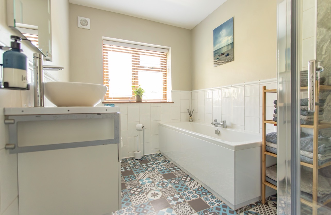 Large bathroom with bath, sink, heated towel rail and patterned floor tiles