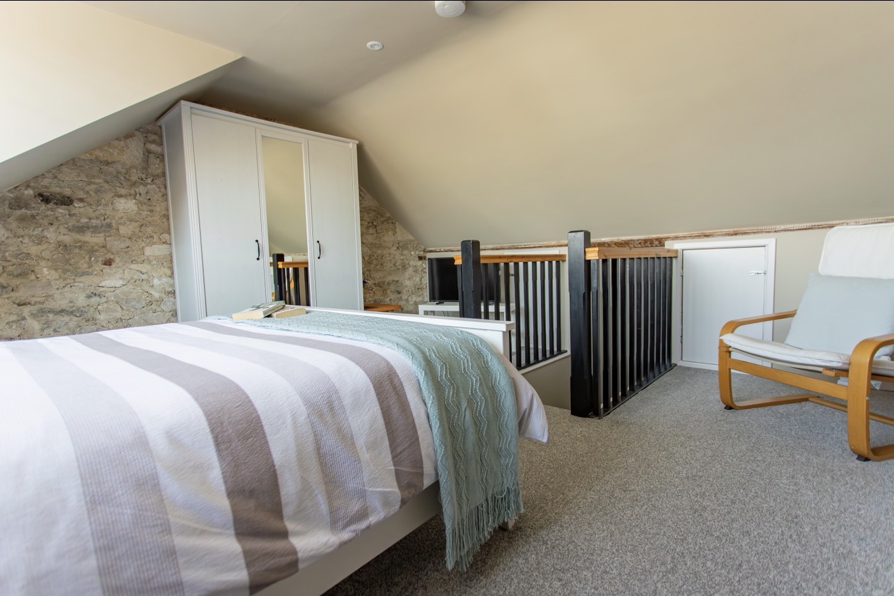 Loft double bedroom with sloped ceiling, exposed stone wall and sea views