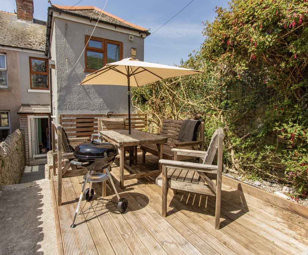 Enclosed cottage garden with wooden decking, outdoor table and chairs, parasol and charcoal BBQ