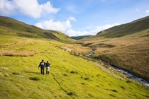 Two people walking in the Cambrian Mountains with a river to their right