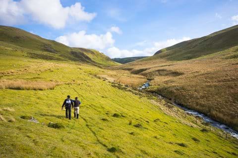 View of two people walking in the Cambrian Mountains with a river to their right